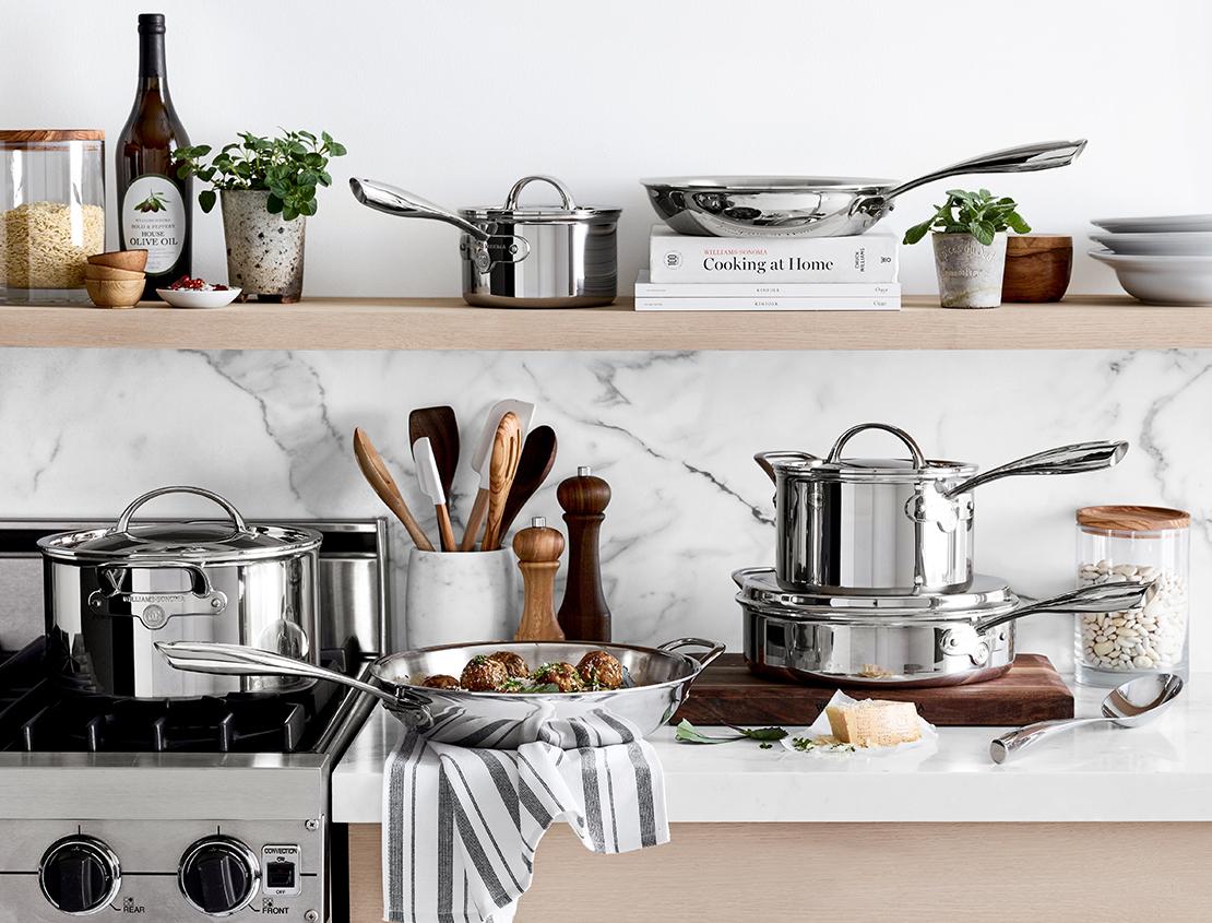 Shop Williams Sonoma — Cookware, Cooks' Tools, Kitchen Appliances & Gourmet Food | Featuring assorted stainless-steel Williams Sonoma cookware and wooden cooks' tools on open wooden shelving and marble countertop in kitchen.